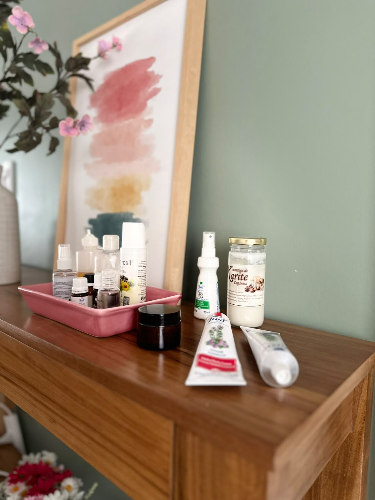 Cuadro de acuarela en tonos rosa, mostaza y verde junto a aceites naturales